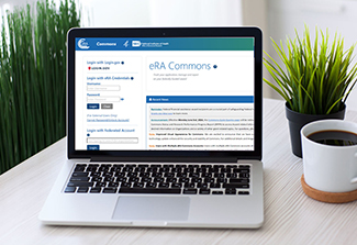 This photo shows a laptop computer on a table; its screen displays the login page for eRA commons.
