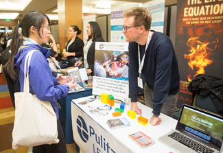 In busy exhibit hall conference attendee talks with exhibit booth staff