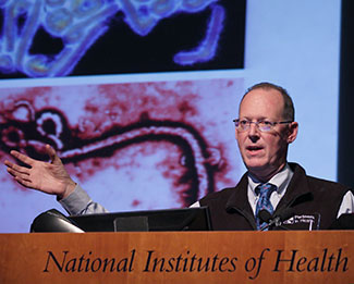 Paul Farmer speaking at a podium at NIH, slide projected in the background