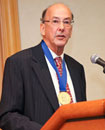 Dr. Roger I. Glass stands at a podium wearing gold medal around his neck