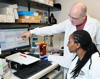 A postdoctoral fellow and a senior investigator, both in lab coats, collaborate around a computer in an NIH lab.