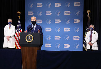 U.S. President Joe Biden speaking at NIH, Dr. Francis Collins and Dr. Anthony Fauci in background.