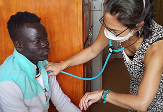 The photo shows Registered Nurse and Ph.D. Abigail Link treating a patient in Northern Uganda