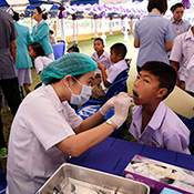 Dr. Waranuch Pitiphat, dressed in a white lab coat, provides dental care to a child. They are pictured seated within a tent where other dentists work with other patients. 