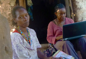 Dr Rachel Idowu seated on doorstoop outside types on laptop, in foreground seated next to her are a woman and children