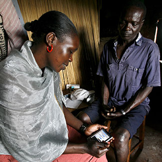 Researcher seated across from a patient enters data on a mobile device.