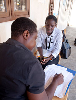 Female researcher collects data with pen and paper from female research participant who is seated across from her