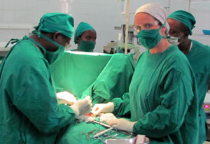 Dr Robin Petroze in green hospital scrubs and mask during a surgery with one additional surgeon, two workers in background