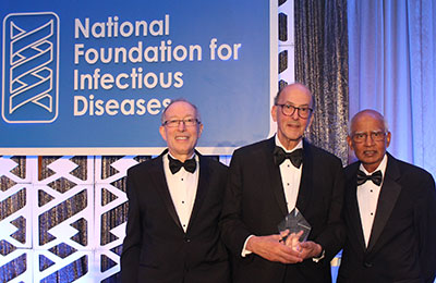 Drs Orenstein, Glass and Santosham in tuxedos stand before a sign reading National Foundation for Infectious Diseases
