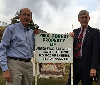 Roger Glass and Francis Collins stand beside a sign outdoors that reads Zika Forest