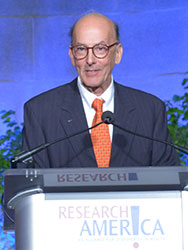 Roger Glass speaks into a microphone at a podium labeled Research!America