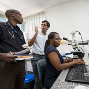 Dr. Satish Gopal talks with UNC-Project Cancer Program staff Tamiwe Tomoka (at microscope) and Edwards Kasonkanji (standing).