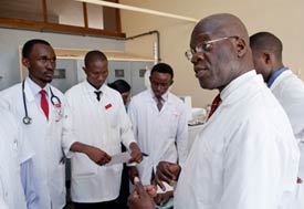 Medical students in white coats listen attentively to speaker, all standing in group in a clinical setting