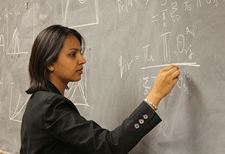 A scientists intently works a complex math problem with chalk on a blackboard
