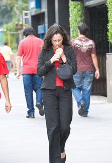 Woman lights cigarette while walking down sidewalk