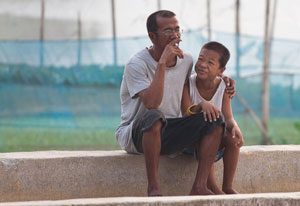 Man smoking cigarette seated outside, arm around young boy