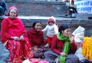 Group of women and child seated outside, one woman smoking a cigarette