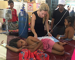 Dr. Jessica Manning works with a child patient in a clinic setting in Cambodia while others look on.