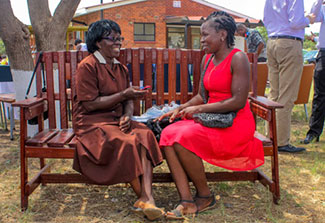Two women sit on a park bench outdoors, facing each other and speaking together