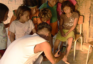 Health worker uses mobile phone app evaluate suspected leishmaniasis lesions on leg of young girl, group of surrounds her.