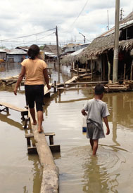 Woman walks on planks propped up over flooded street, boy walks on street next to her in water up to his knees