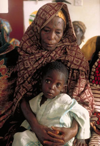 Mother looking down sits with young child on her lap, child looks at camera