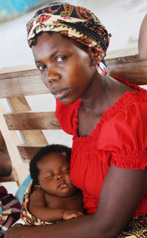 Mother looks directly at camera while holding a sleeping baby