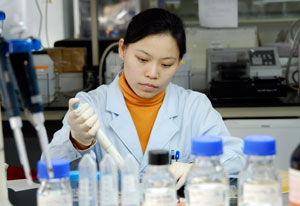 Woman in white lab coat surrounded by bottles and containers tops on concentrates as she put a sample in a container