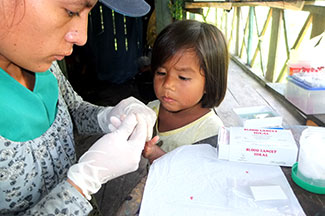 Medical worker administers fingerstick blood test on young girl in Peru