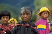 In Bhutan, one older woman and one younger woman with young child strapped to back, another young child held on hip by person of