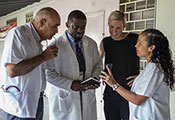 Dr. Bill Pape reviews information on a mobile device with three researchers in a hallway in Haiti