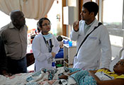 Dr. Omar Siddiqi stands next to bedside of patient, speaks with patient's family and another medical worker.
