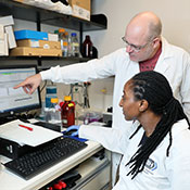 A postdoctoral fellow and a senior investigator, both in lab coats, collaborate around a computer in an NIH lab.