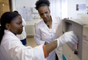 Two female researchers working in a lab, younger one works with equipment, older one by her side observes