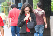 Woman lights cigarette while walking down sidewalk