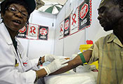 Photo by Paballo Thekiso/AFP/Getty Images. Female health worker performs a blood test on a man, stop AIDS posters on the wall.