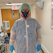 Dr. Mark Brady stands in the hallway of a hospital wearing full PPE, including a hair net, half-mask respirator, suit and gloves.