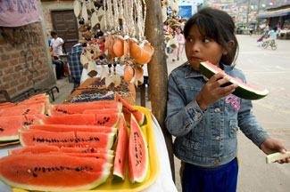 Latin American girl eats watermelon outside a street vendor stall