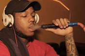 Young man exhales smoke after inhaling from hose of a waterpipe, wearing large headphones and baseball cap