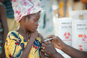 Young girl in outdoor clinic holds up sleeve to receive shot in the upper arm, healthcare worker off camera