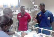 Dr Rockafeller Oteng speaks with others standing at bedside of a patient in a hospital bed