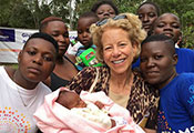 NICHD Director Dr. Diana Bianchi, center holding a baby, surrounded by young people in Kenya.