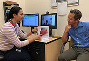 Dr. Nauzley Abedini seated at a desk in office, points to a model of a liver, discusses with person seated across from her.