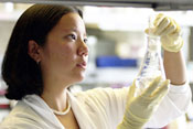 Female researcher in lab holds up and observes contents of a flask