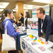 Photo by Ross Marlow for CUGH, in busy exhibit hall conference attendee talks with exhibit booth staff