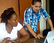 In office, Dr. Eric Coker standing works on a tablet while woman working with a smartphone looks on.