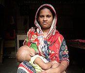 Woman seated indoors breastfeeds a baby.