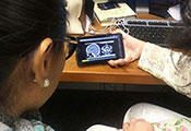 Two researchers seated with backs to camera in front of a computer view a video of brain scans on a mobile device