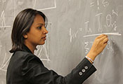 A scientists intently works a complex math problem with chalk on a blackboard