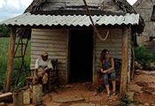 Older man and younger student seated in front of small farm house in Cuba